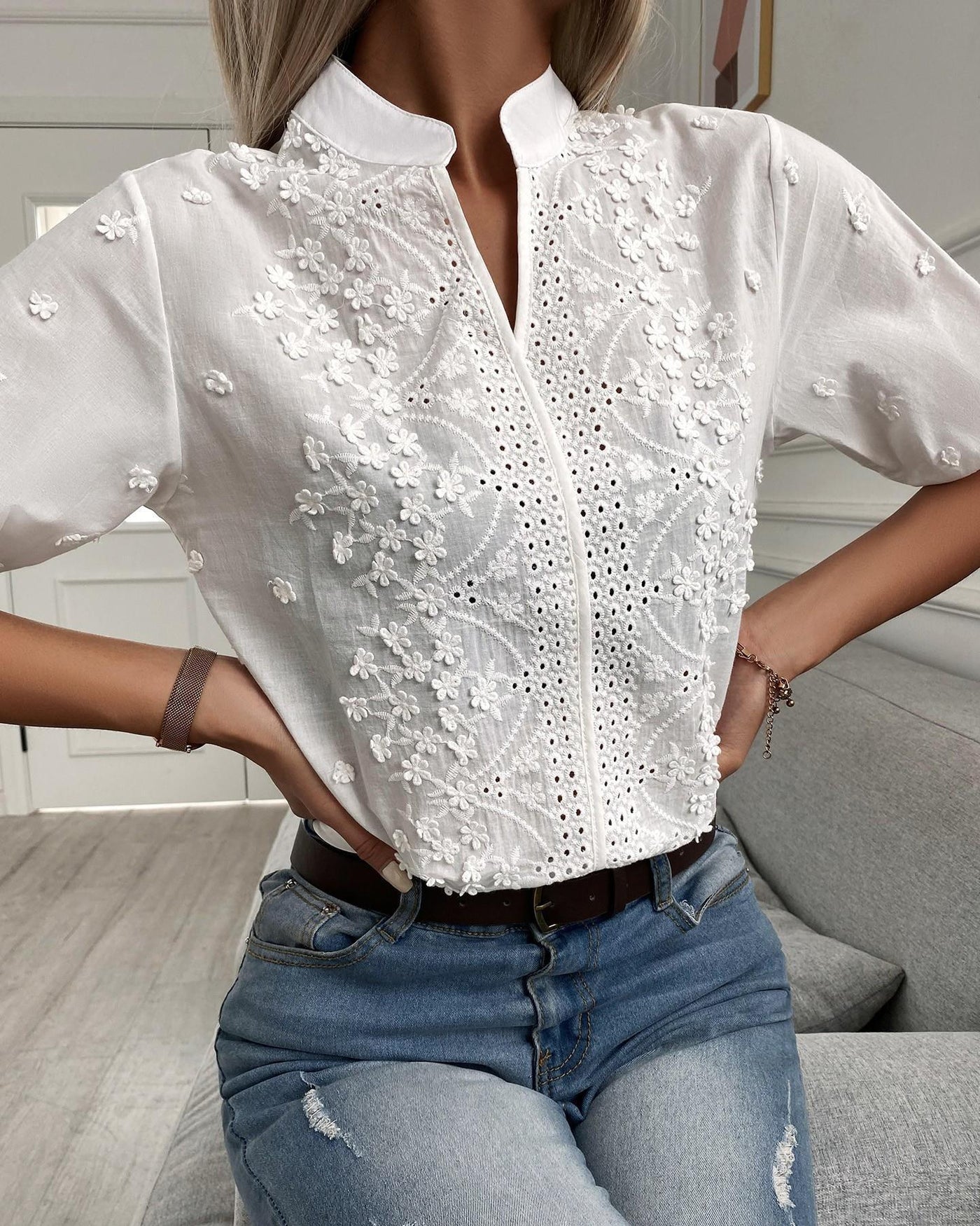 Person wearing a white embroidered blouse and blue jeans in an indoor setting
